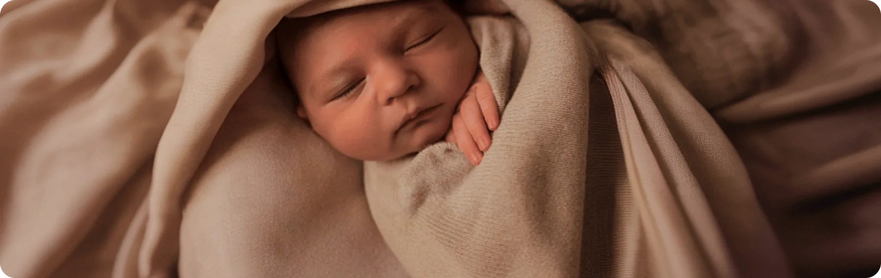 Bebê recém-nascido dorme envolto em uma manta